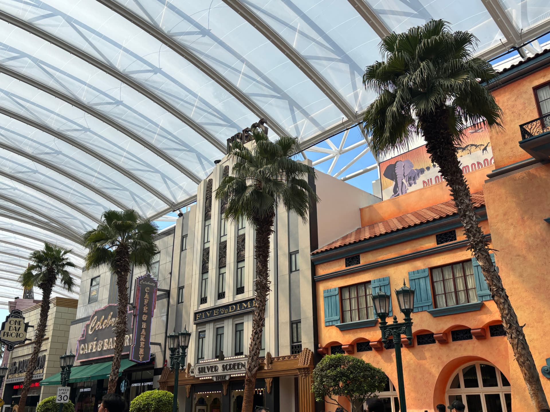 Palm-lined street and colourful building facades beneath a glass canopy