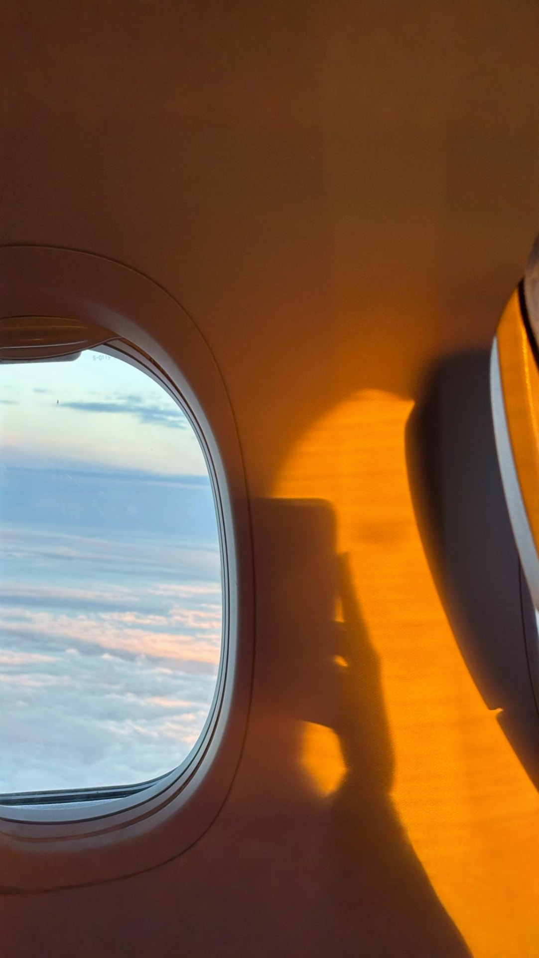 Clouds and evening sky through an airplane window, with golden light across the cabin wall